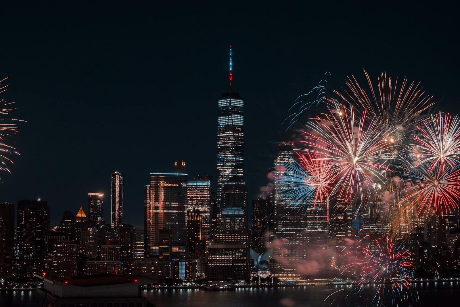New York City skyline at night with red and white Fourth of July fireworks bursting over the East River