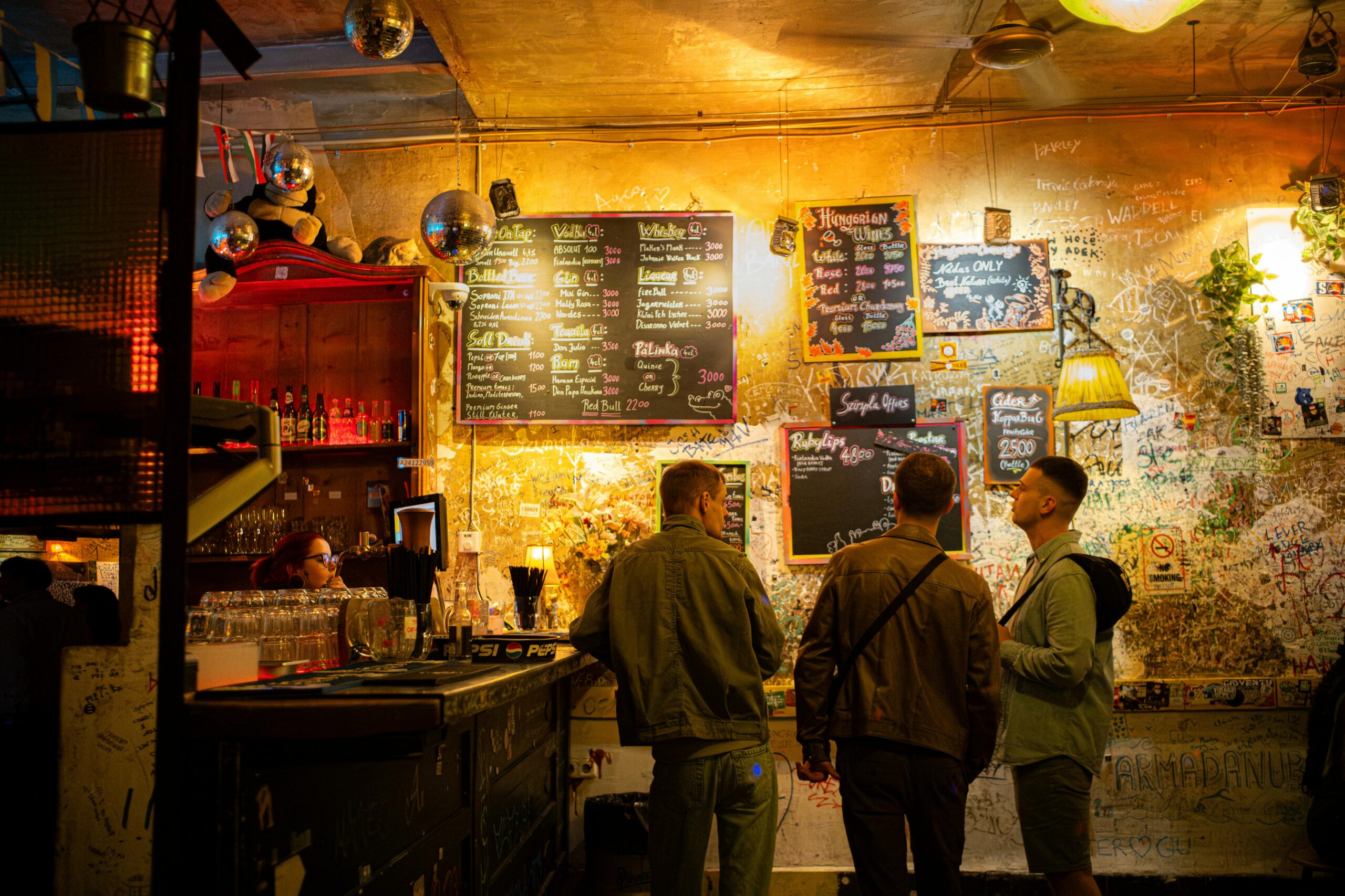 Ruin bar interior in Budapest's Jewish Quarter — warm orange lighting, graffiti walls, and chalkboard menus